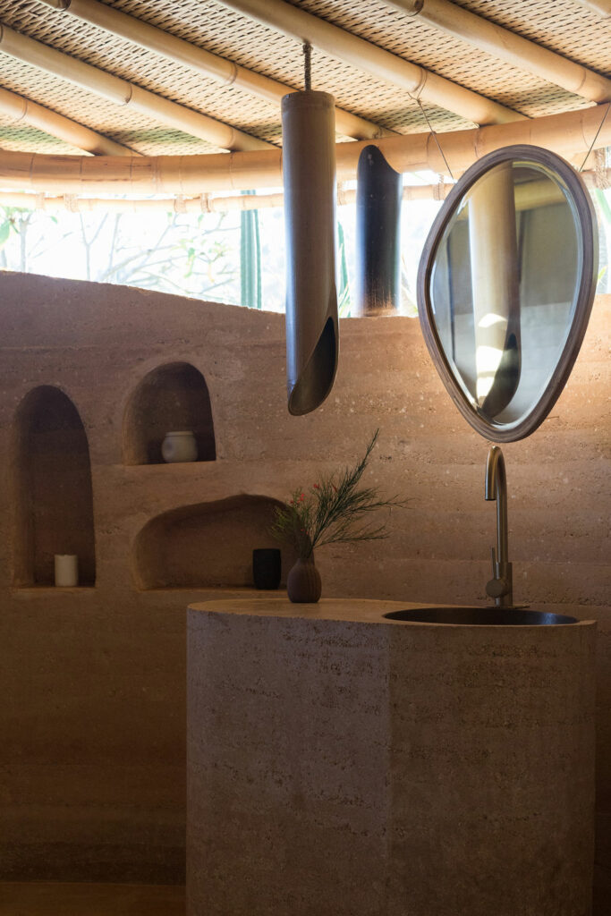 Round mirror on a sculpted earthen wall in a tent suite bathroom in Bali.